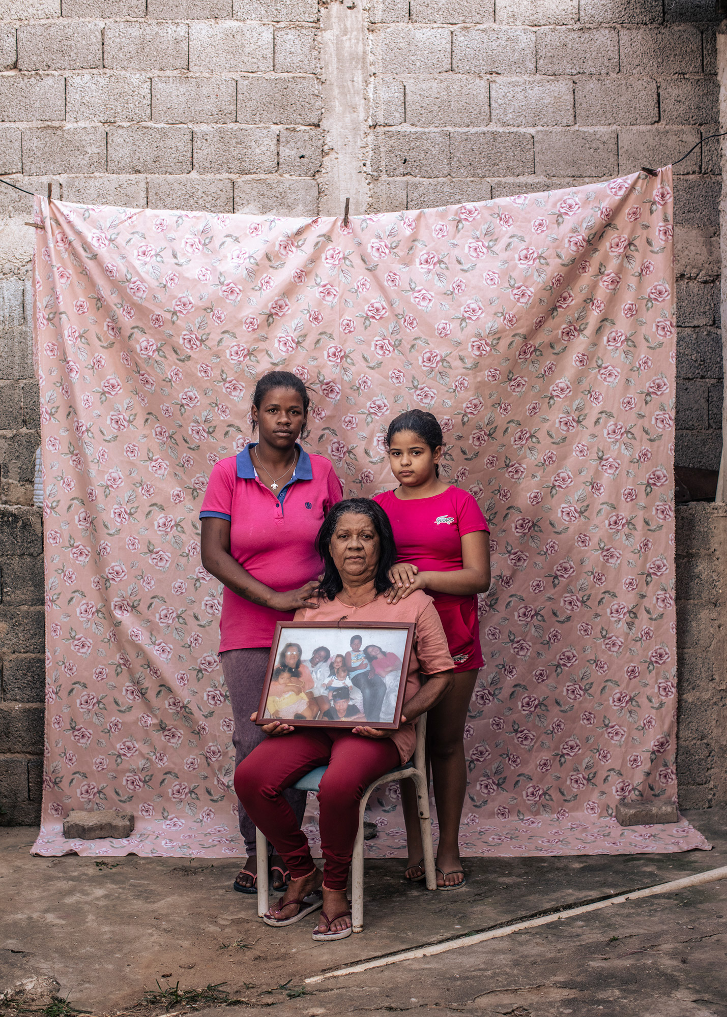 Portrait of Isabel and her granddaughters holding a picture of their family. All missing members are in prison.  